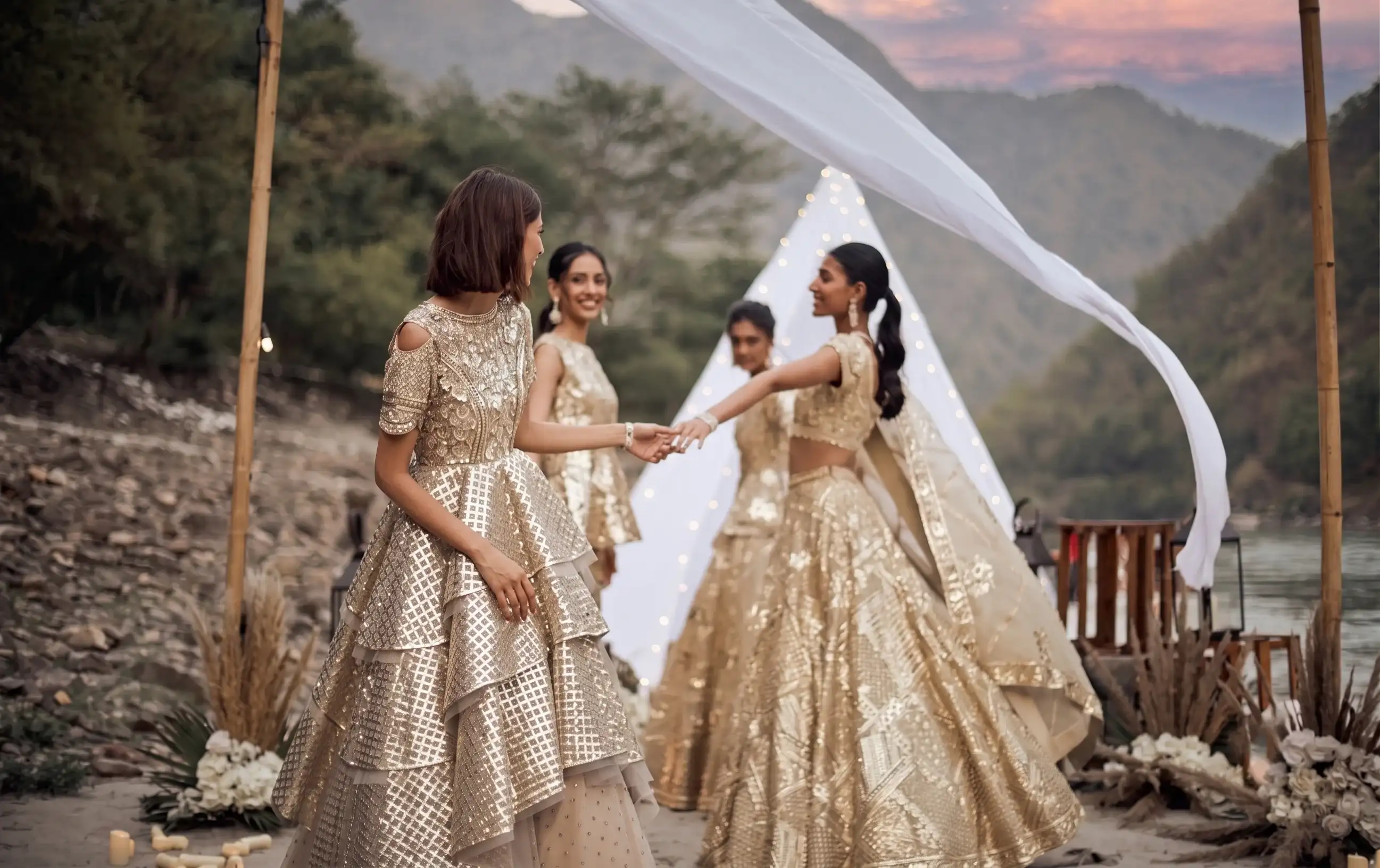 Bridesmaids in gold lehengas dancing by the river at dusk