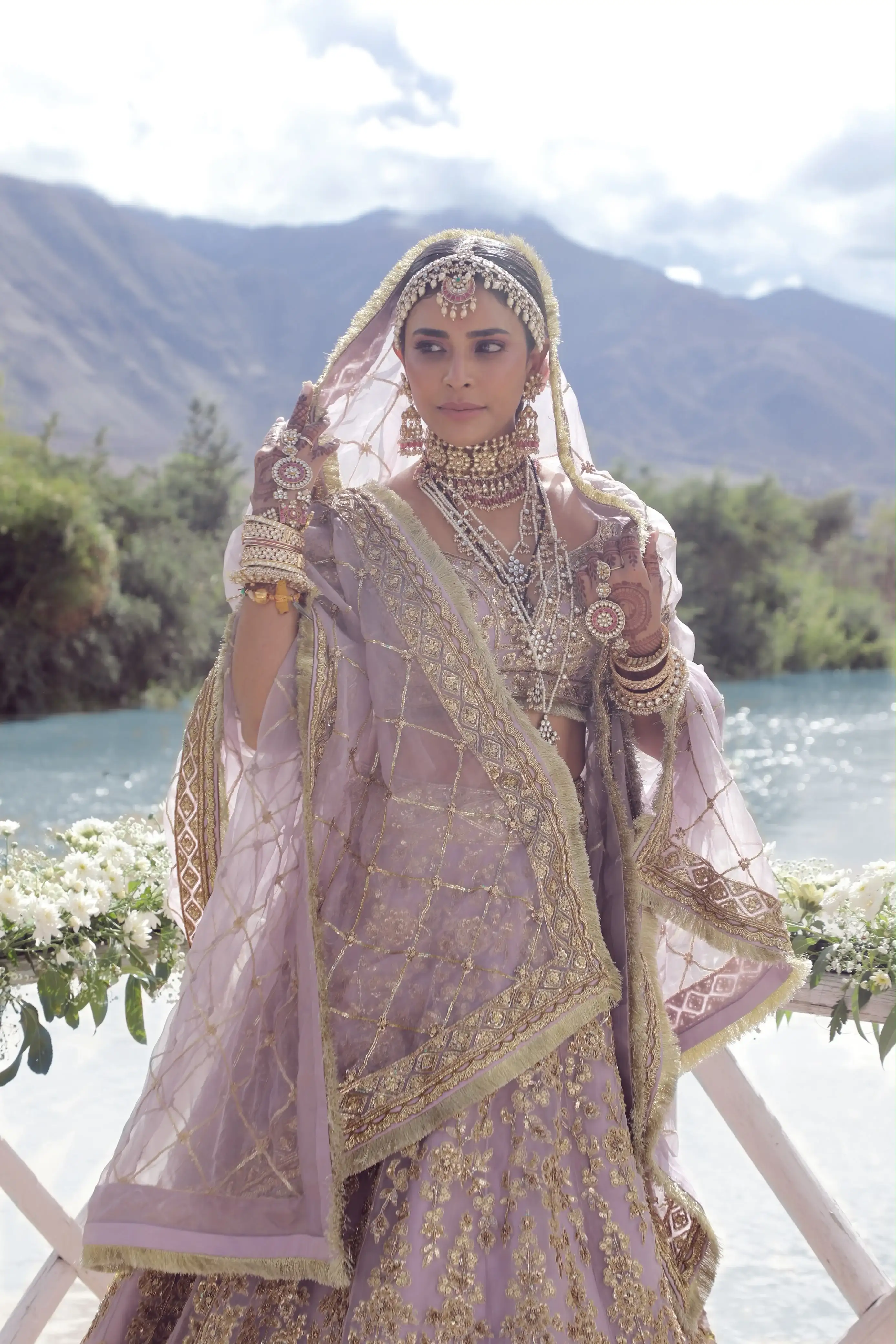 Bride lifting her embroidered dupatta by the lake