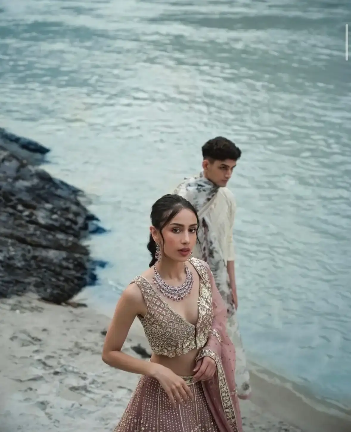Couple in a blush lehenga and floral sherwani by the river's edge